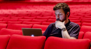 a man sitting inside an empty theatre with his laptop