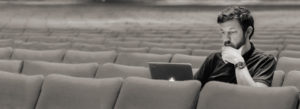 man on laptop sitting alone inside a theatre